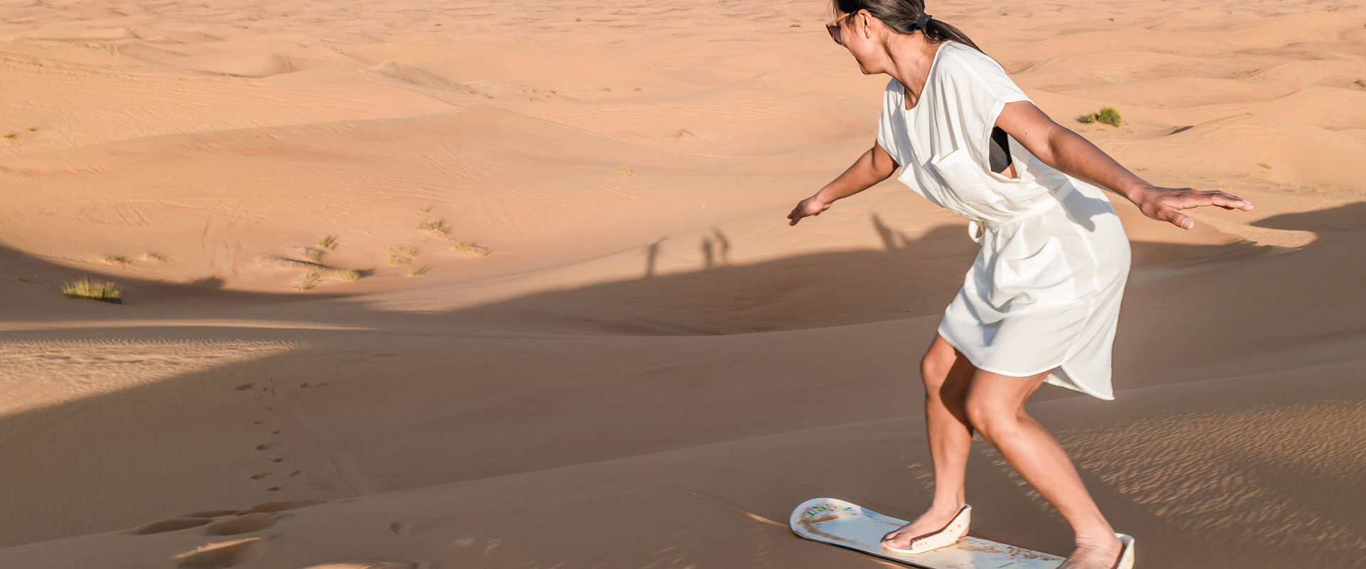 A guest sandboarding on Dubai's golden desert dunes